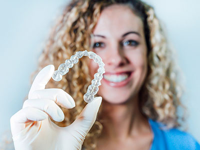 A woman holding up a clear dental retainer with her right hand against a white background.