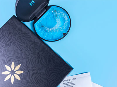 A blue toothbrush with bristles inside an open box, placed on a surface next to a closed black box and a booklet with a floral pattern cover.
