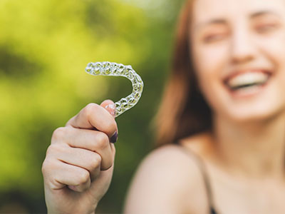 The image shows a person holding up a transparent toothbrush with bristles towards the camera, smiling at the viewer.