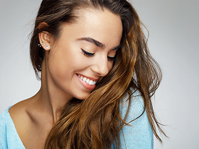 A smiling woman with long hair, looking down and to her left, against a light background.