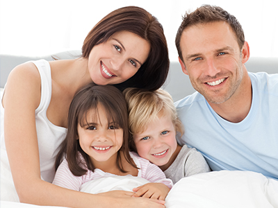 A family of four posing for a picture on a bed with white sheets.