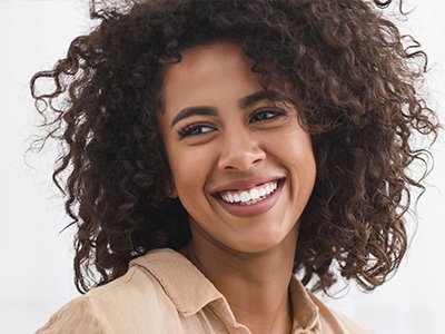 A smiling woman with curly hair, wearing a cream top, against a white background.